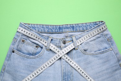 Photo of Jeans and measuring tape on green background, top view