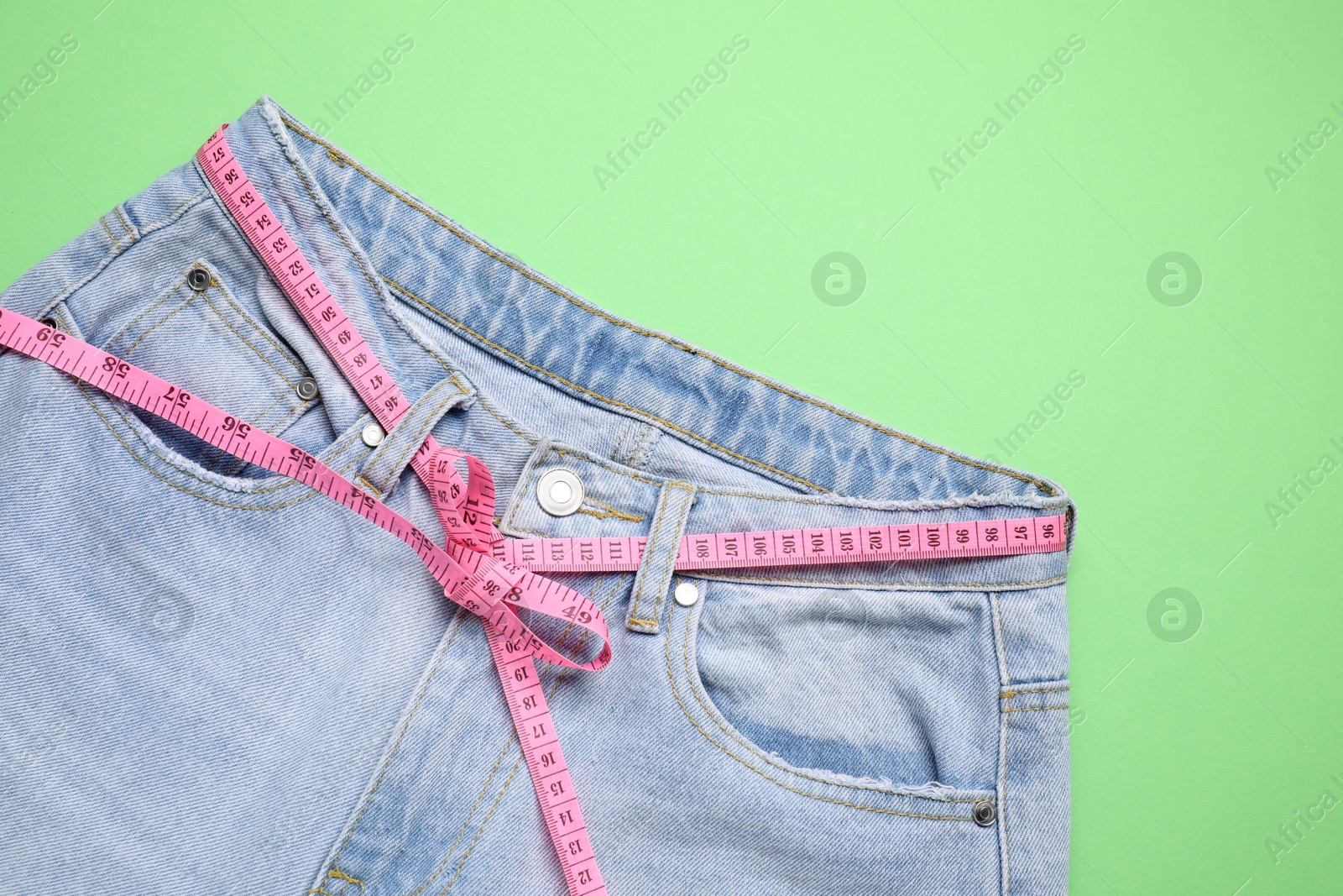 Photo of Jeans and measuring tape on green background, top view