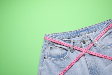 Photo of Jeans and measuring tape on green background, top view. Space for text