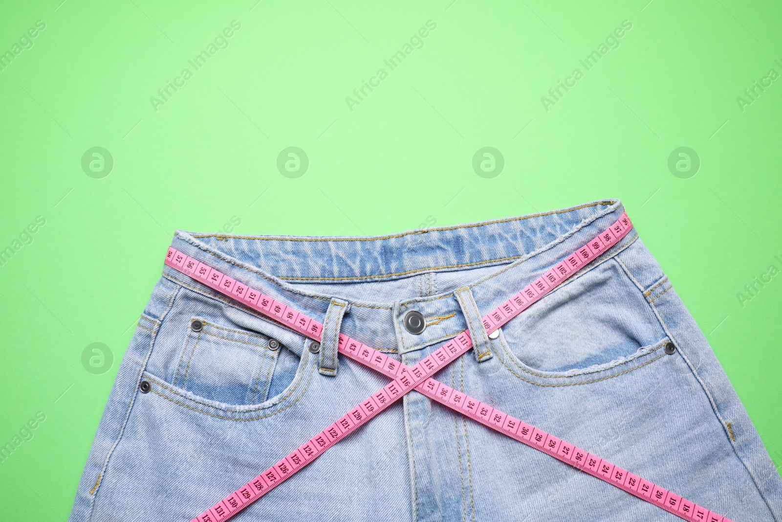 Photo of Jeans and measuring tape on green background, top view