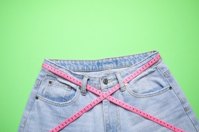 Photo of Jeans and measuring tape on green background, top view