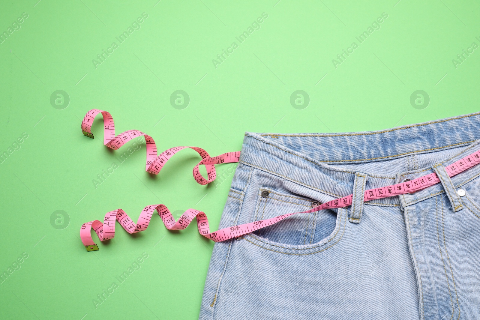 Photo of Jeans and measuring tape on green background, top view