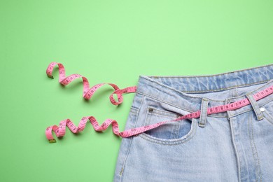 Photo of Jeans and measuring tape on green background, top view