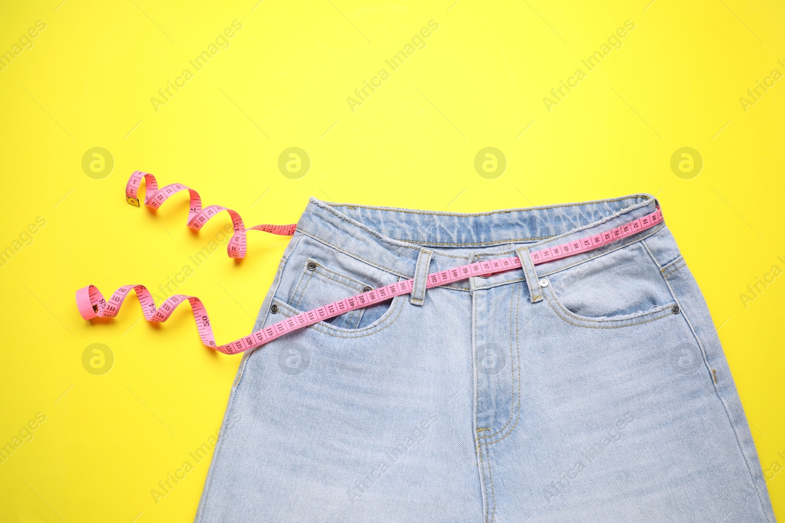 Photo of Jeans and measuring tape on yellow background, top view