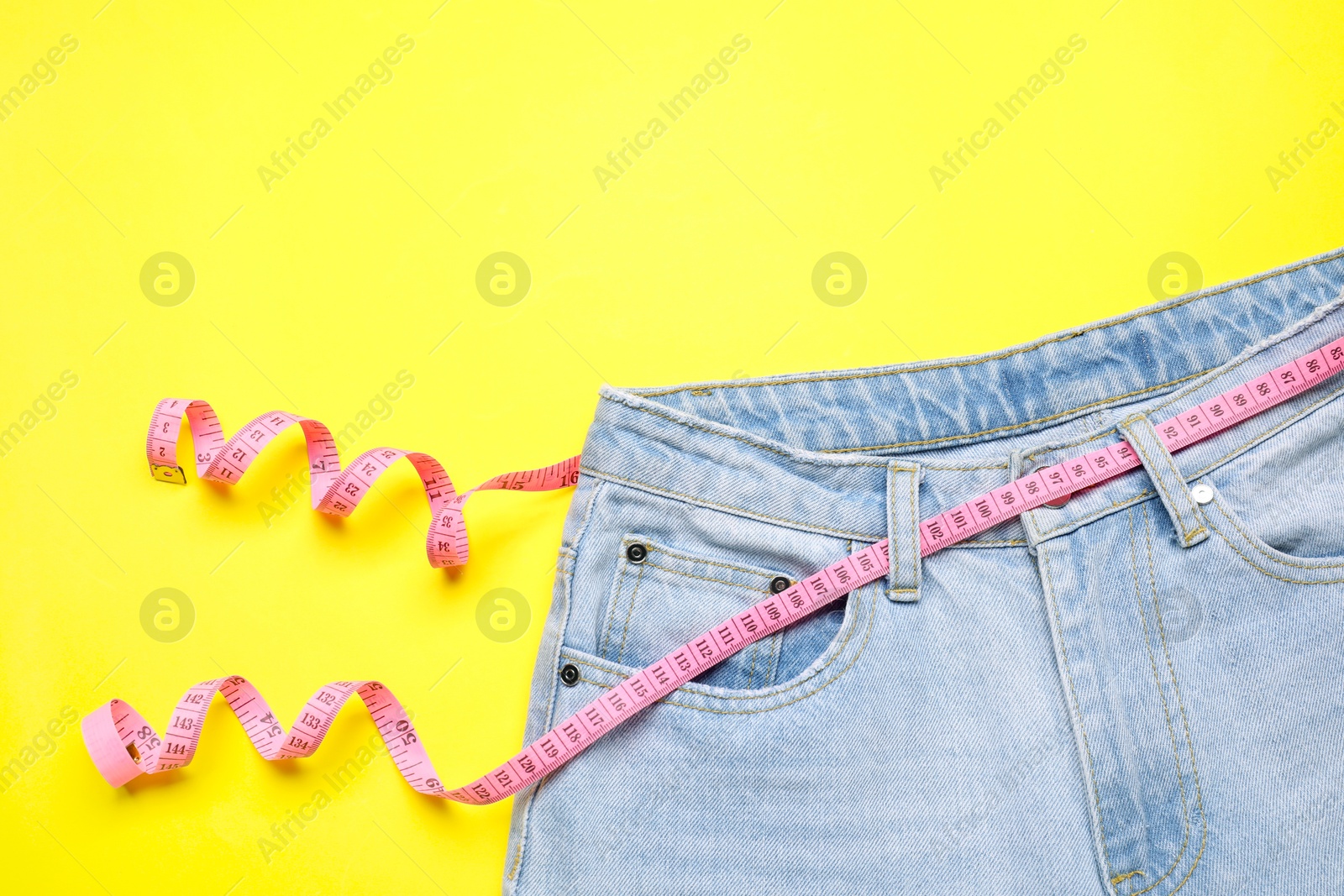 Photo of Jeans and measuring tape on yellow background, top view