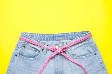 Photo of Jeans and measuring tape on yellow background, top view