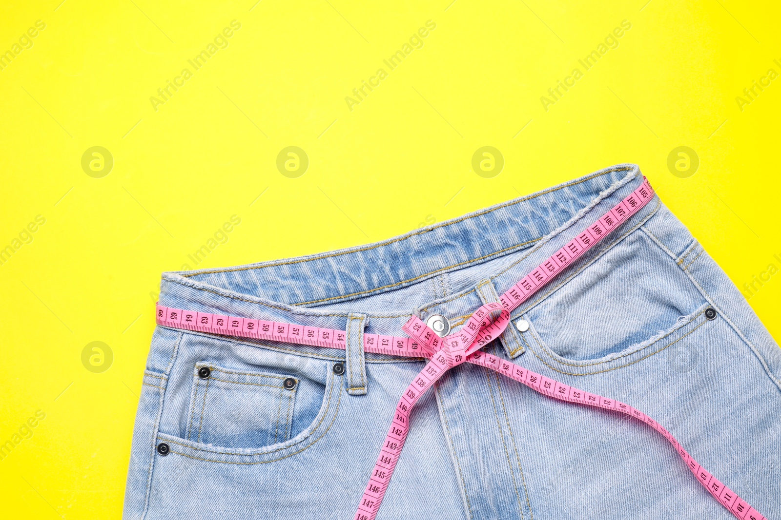 Photo of Jeans and measuring tape on yellow background, top view