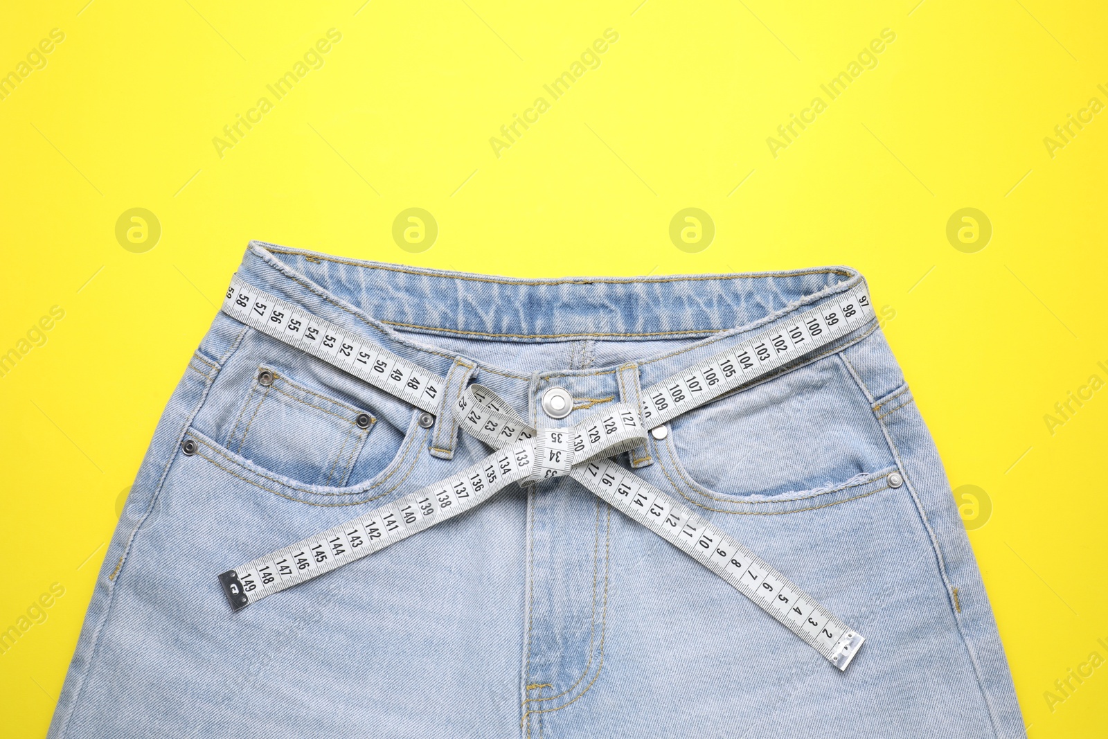 Photo of Jeans and measuring tape on yellow background, top view