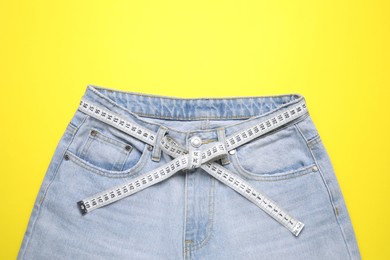 Photo of Jeans and measuring tape on yellow background, top view