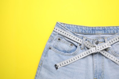 Photo of Jeans and measuring tape on yellow background, top view. Space for text