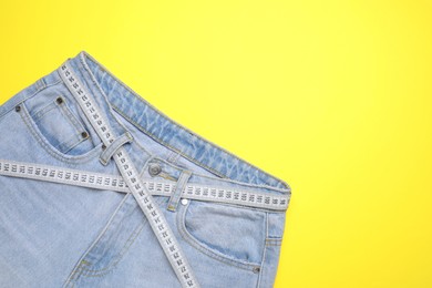 Photo of Jeans and measuring tape on yellow background, top view. Space for text