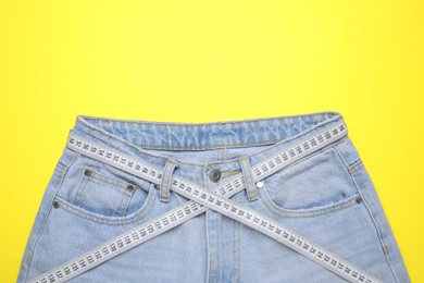 Photo of Jeans and measuring tape on yellow background, top view