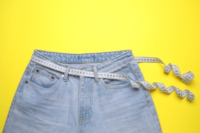 Photo of Jeans and measuring tape on yellow background, top view