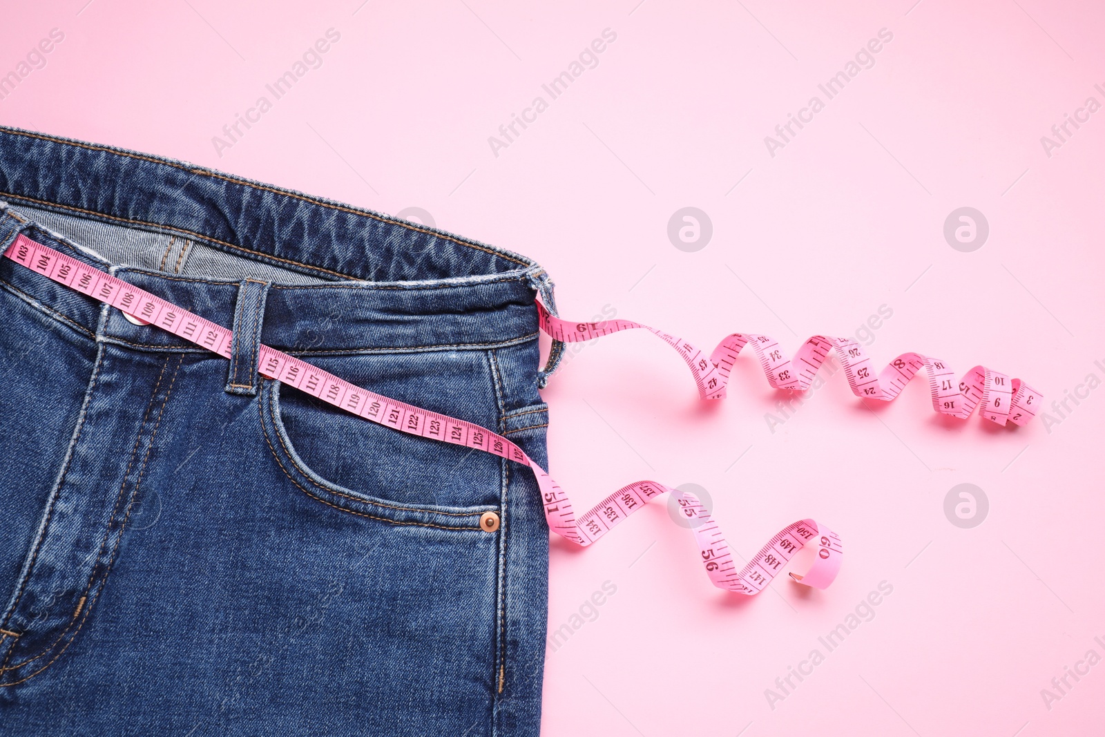 Photo of Jeans and measuring tape on pink background, top view. Space for text