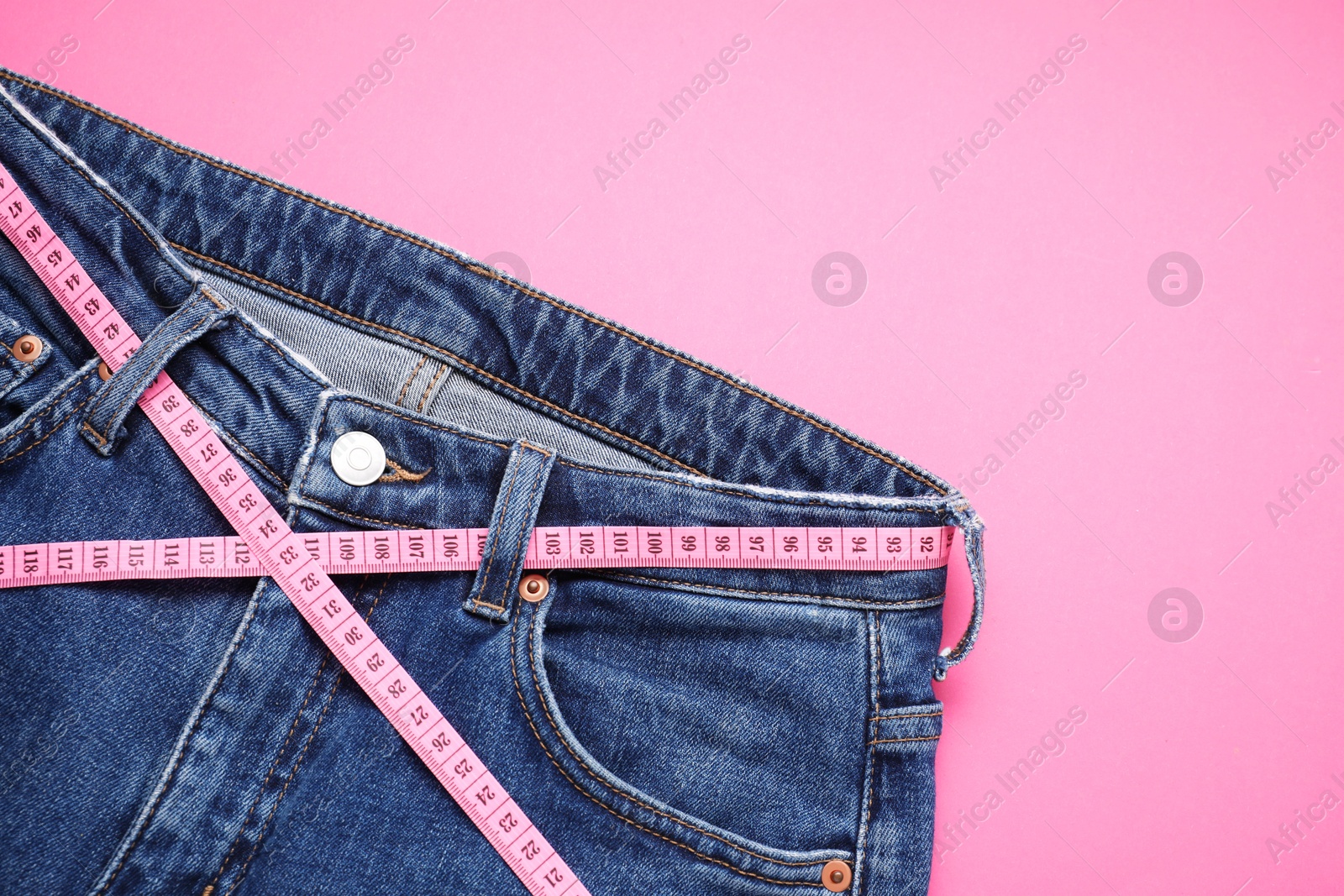 Photo of Jeans and measuring tape on pink background, top view