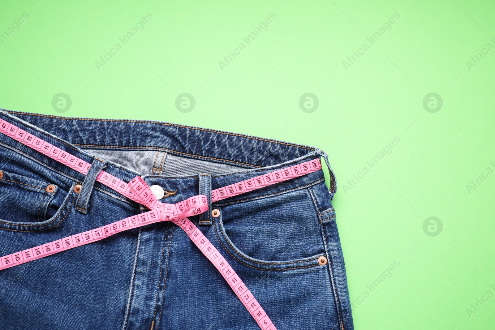 Photo of Jeans and measuring tape on light green background, top view. Space for text