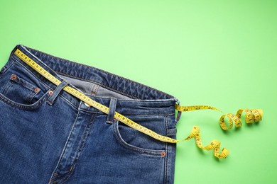 Photo of Jeans and measuring tape on light green background, top view. Space for text