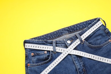 Photo of Jeans and measuring tape on yellow background, top view. Space for text