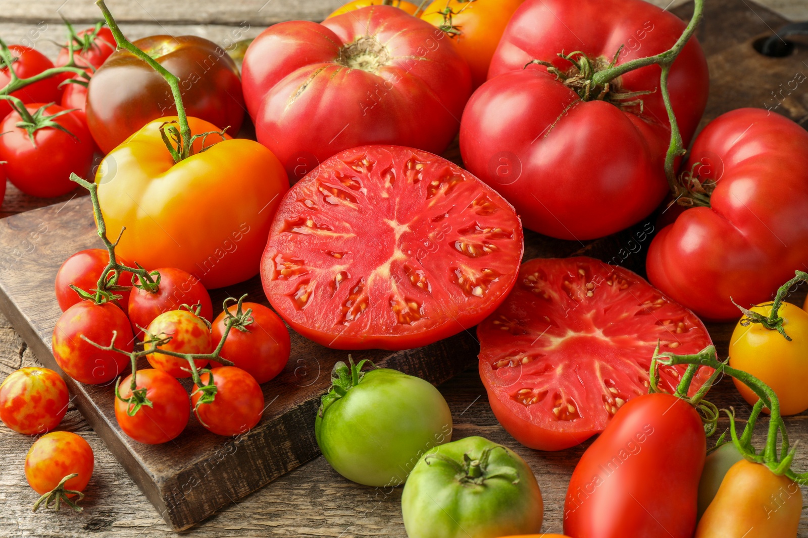 Photo of Many different ripe tomatoes on wooden table, closeup