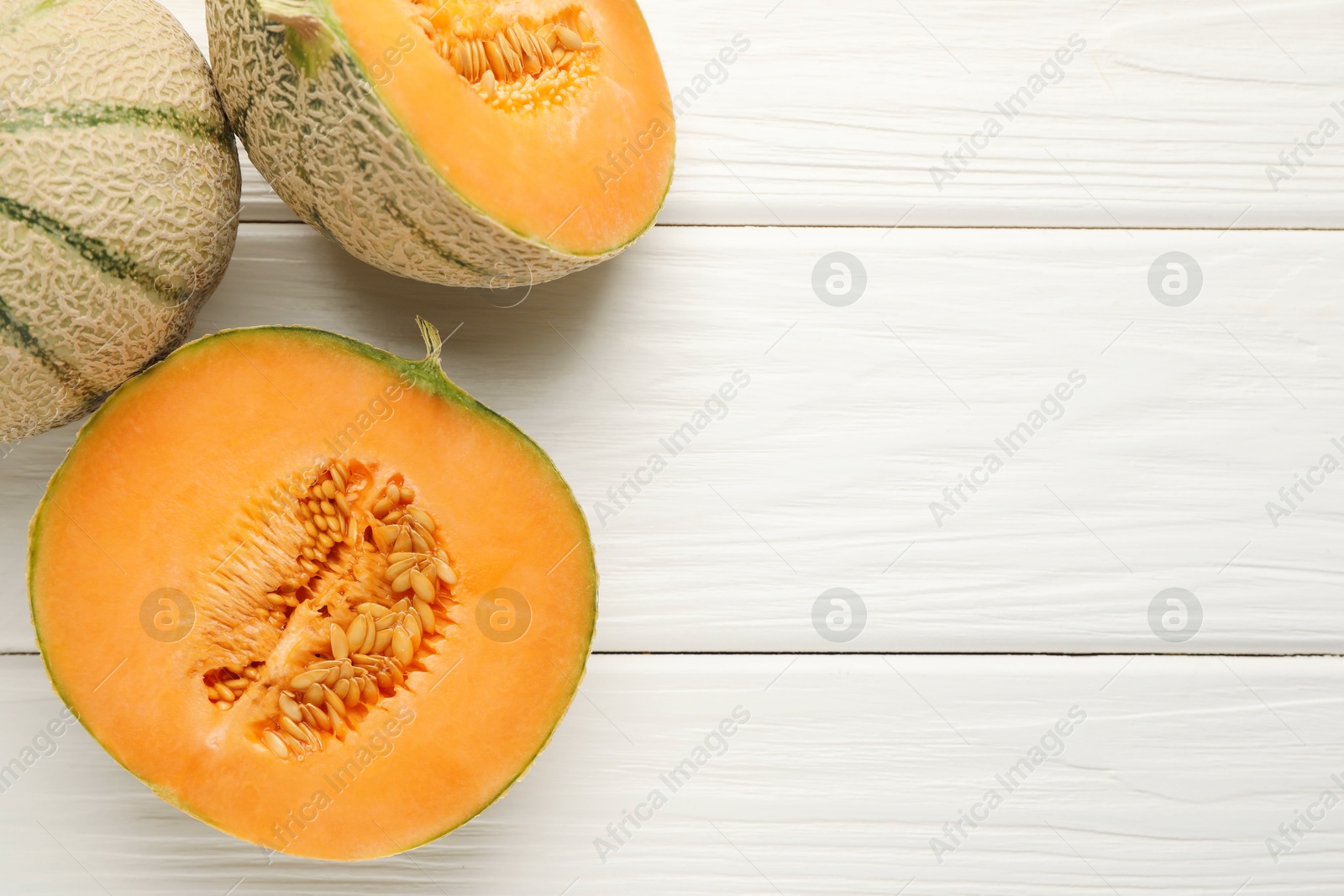 Photo of Whole and cut ripe Cantaloupe melons on white wooden table, flat lay. Space for text