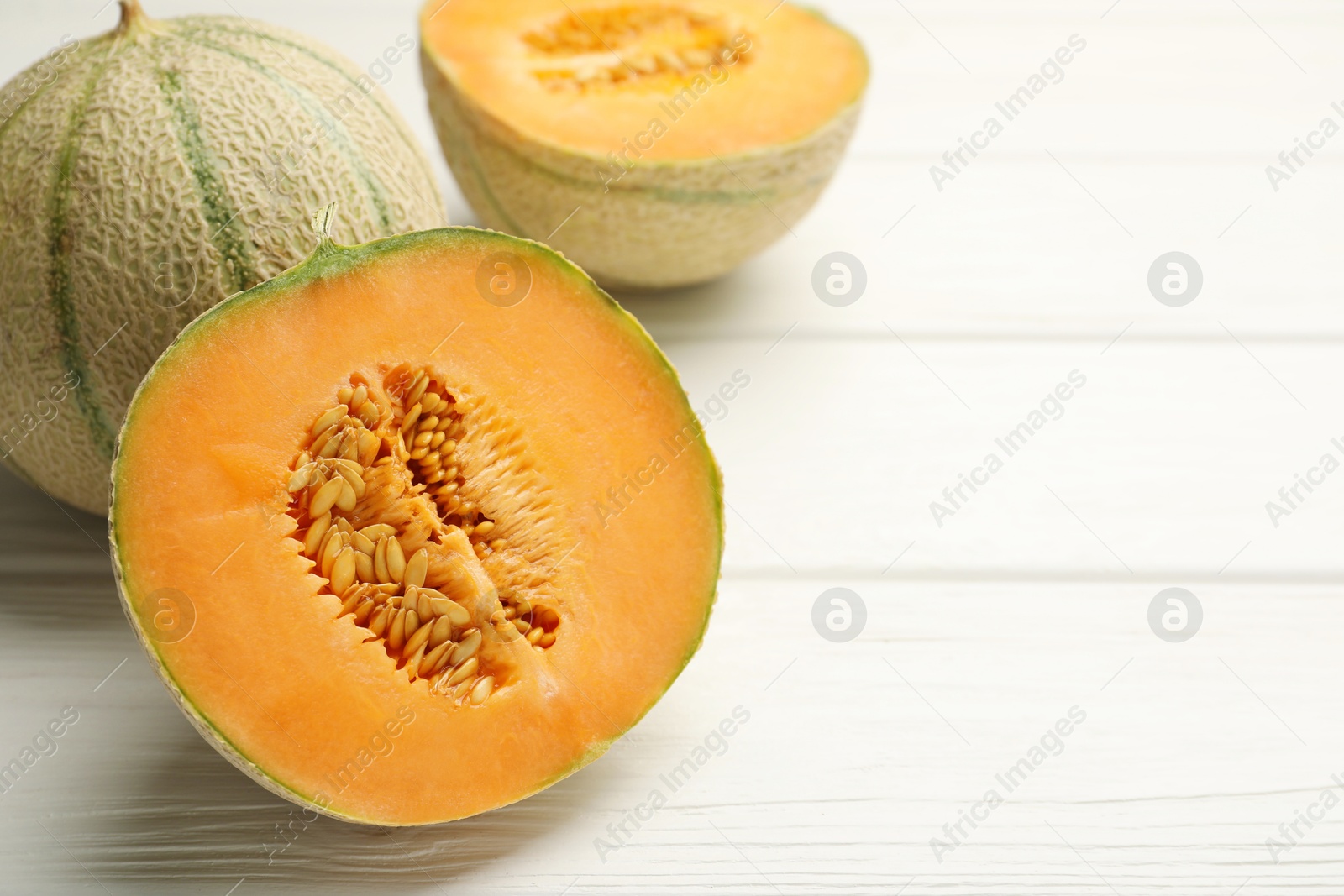 Photo of Whole and cut ripe Cantaloupe melons on white wooden table, closeup. Space for text