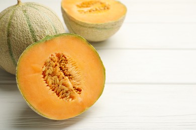 Whole and cut ripe Cantaloupe melons on white wooden table, closeup. Space for text