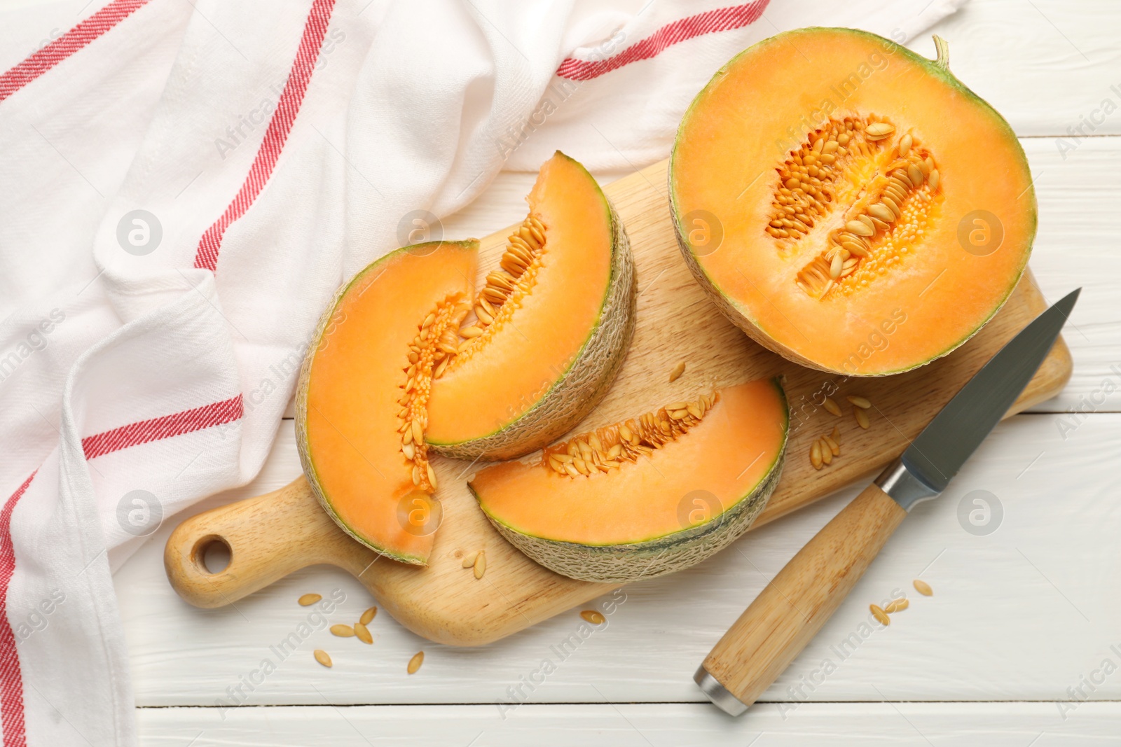 Photo of Cut ripe Cantaloupe melon and knife on white wooden table, flat lay