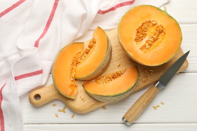 Photo of Cut ripe Cantaloupe melon and knife on white wooden table, flat lay