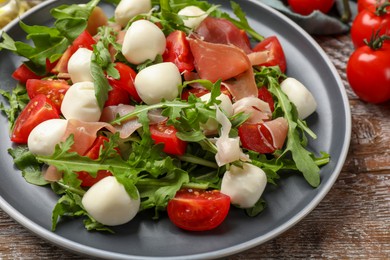 Photo of Tasty salad with arugula, mozzarella cheese, tomatoes and jamon on wooden table, closeup