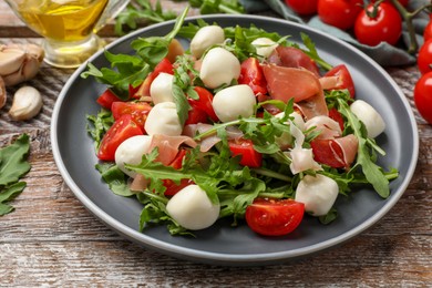 Photo of Tasty salad with arugula, mozzarella cheese, tomatoes and jamon on wooden table, closeup