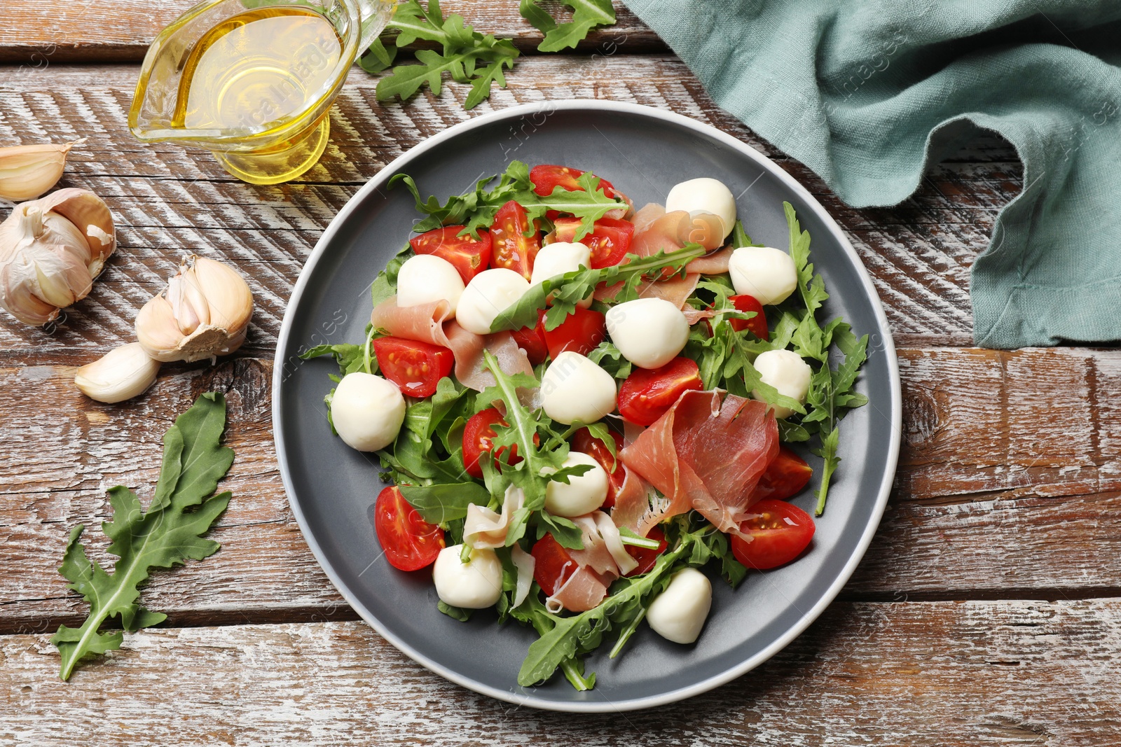 Photo of Tasty salad with arugula, mozzarella cheese, tomatoes and jamon on wooden table, flat lay