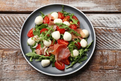 Photo of Tasty salad with arugula, mozzarella cheese, tomatoes and jamon on wooden table, top view