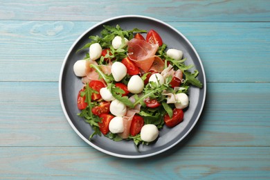 Photo of Tasty salad with arugula, mozzarella cheese, tomatoes and jamon on light blue wooden table, top view