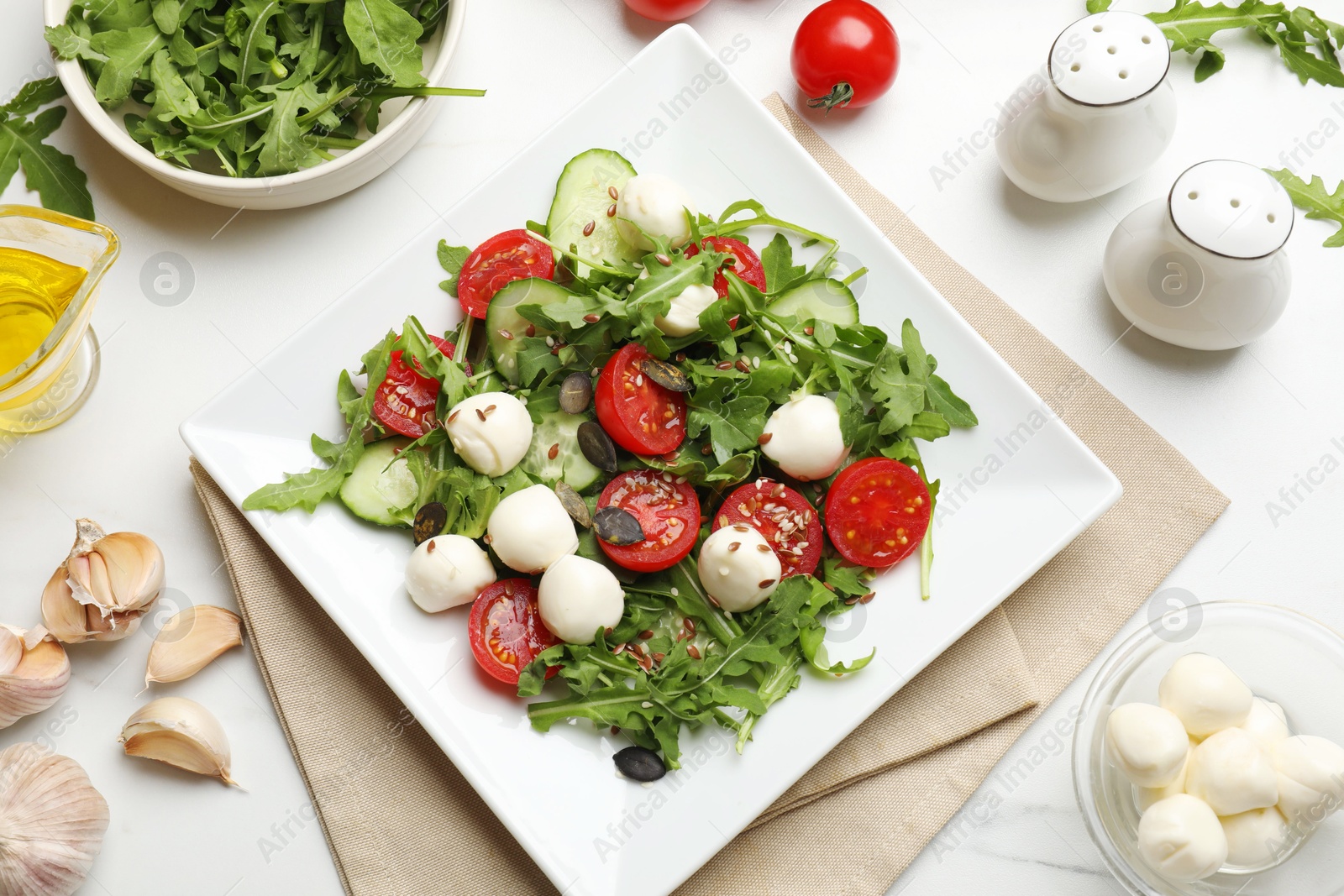 Photo of Tasty salad with arugula, mozzarella cheese and vegetables on white table, flat lay