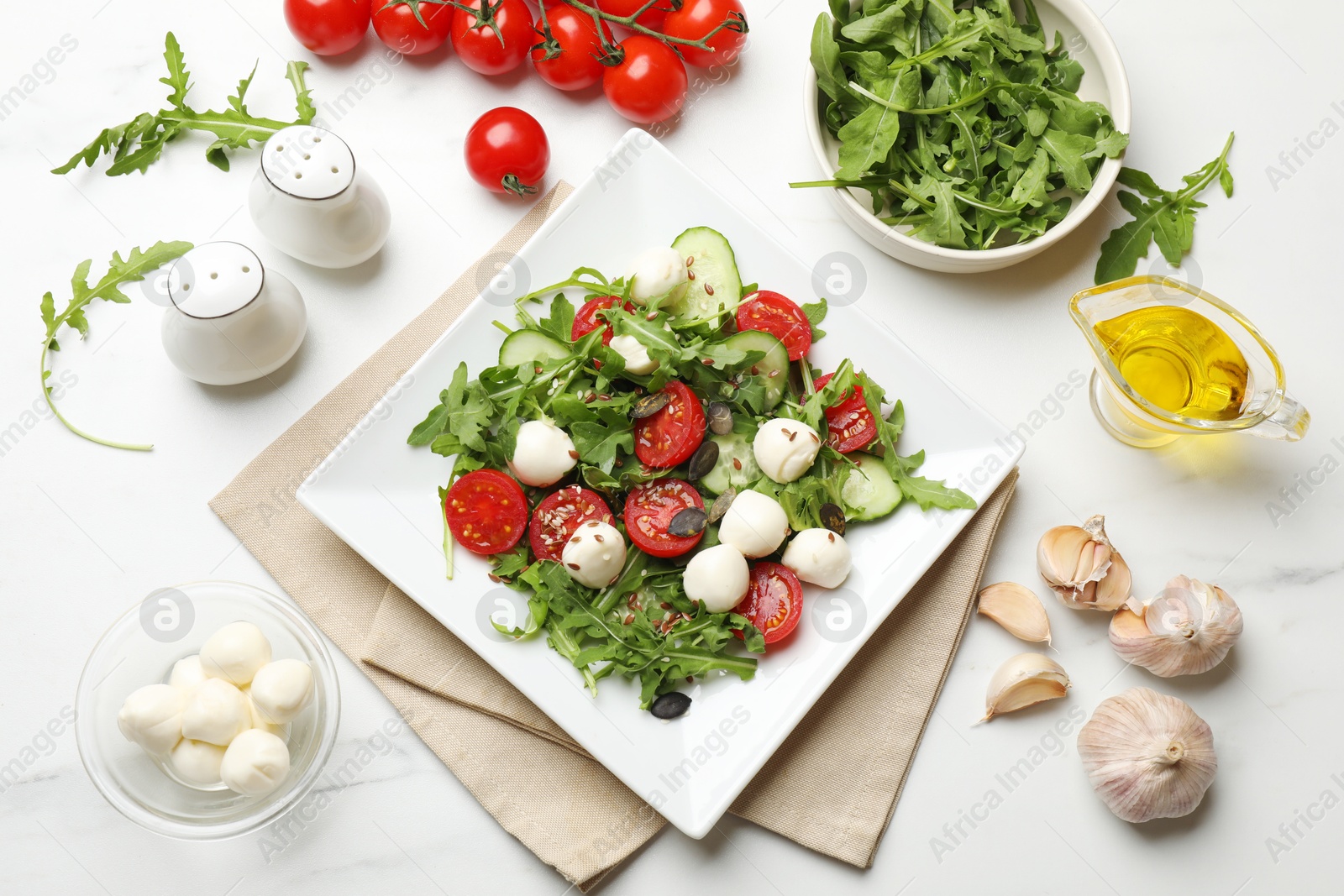 Photo of Tasty salad with arugula, mozzarella cheese and vegetables on white table, flat lay