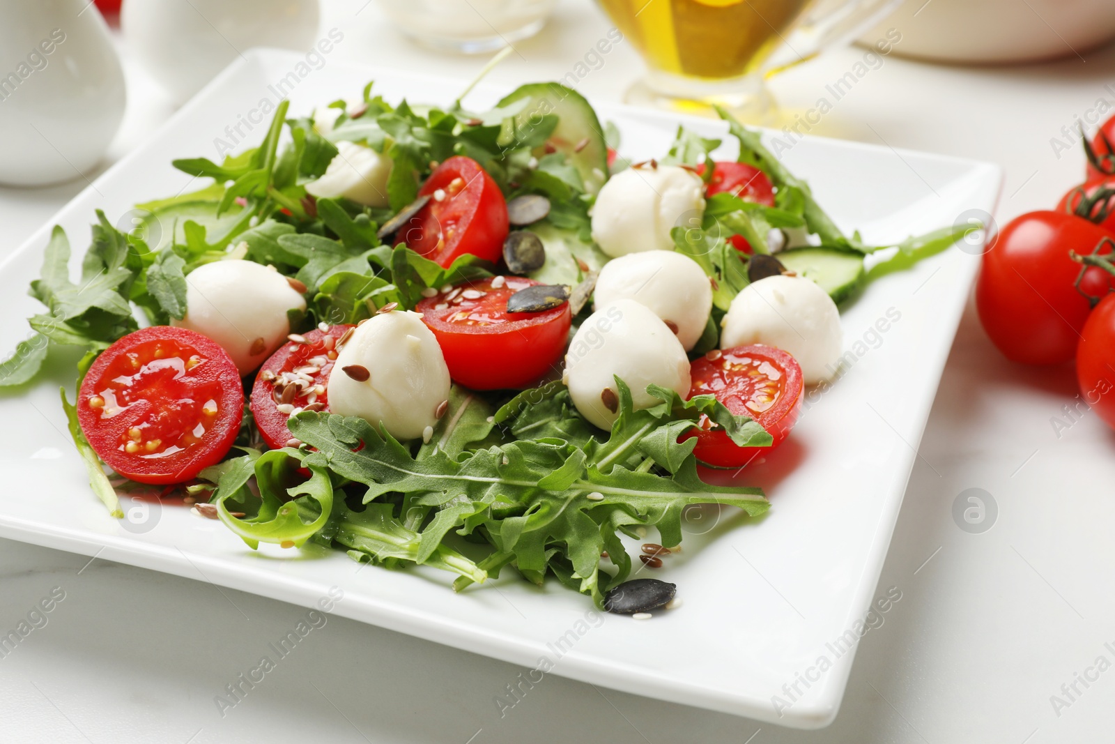 Photo of Tasty salad with arugula, mozzarella cheese and vegetables on white table, closeup