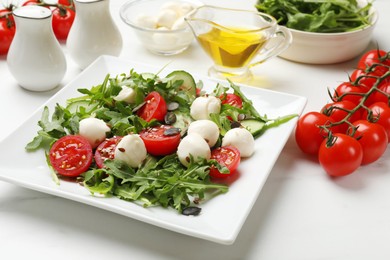 Photo of Tasty salad with arugula, mozzarella cheese and vegetables on white table, closeup