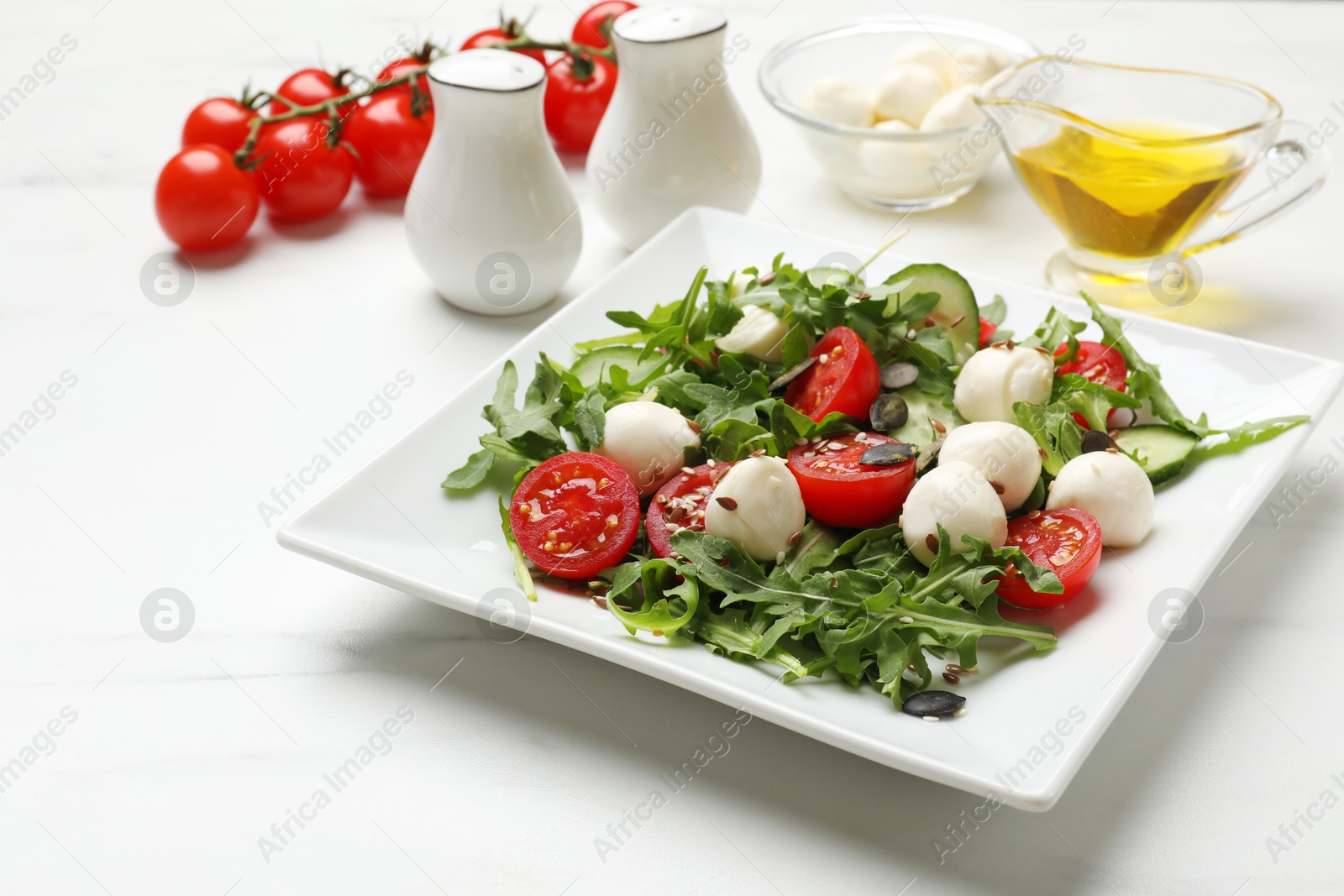 Photo of Tasty salad with arugula, mozzarella cheese and vegetables on white table, closeup