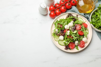 Photo of Tasty salad with arugula, lettuce, mozzarella cheese and vegetables on white table, flat lay. Space for text