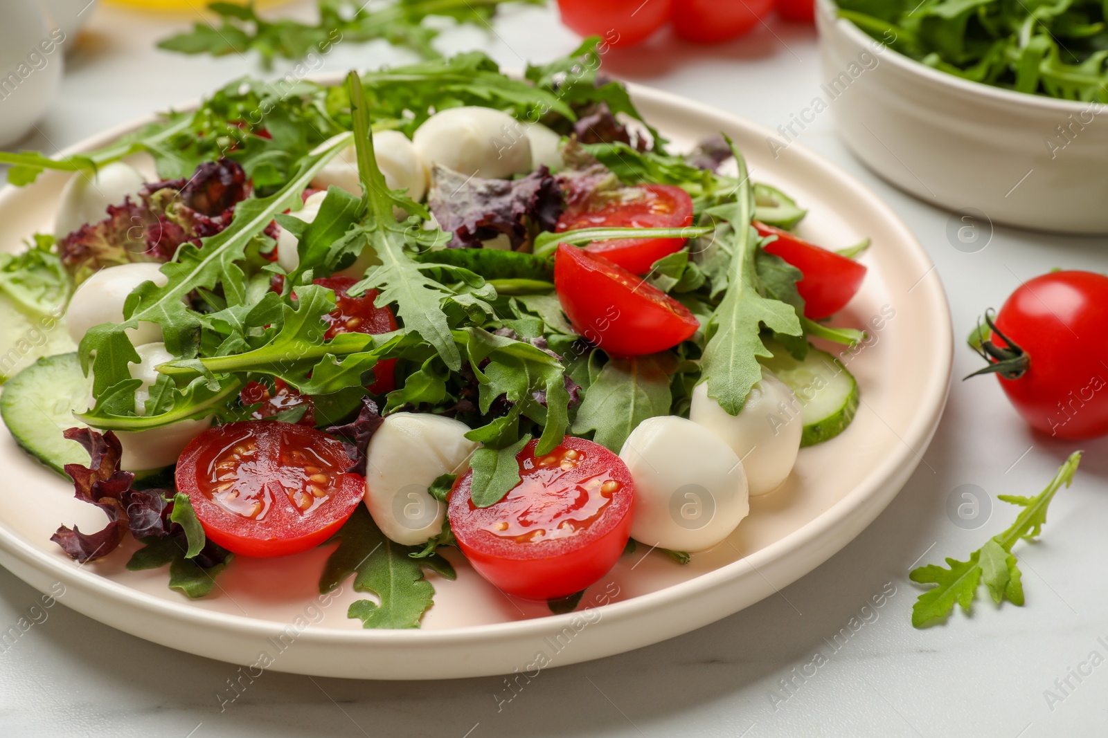 Photo of Tasty salad with arugula, lettuce, mozzarella cheese and vegetables on white table, closeup