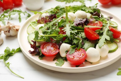 Photo of Tasty salad with arugula, lettuce, mozzarella cheese and vegetables on white table, closeup