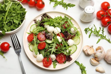 Photo of Tasty salad with arugula, lettuce, mozzarella cheese, vegetables and fork on white table, flat lay