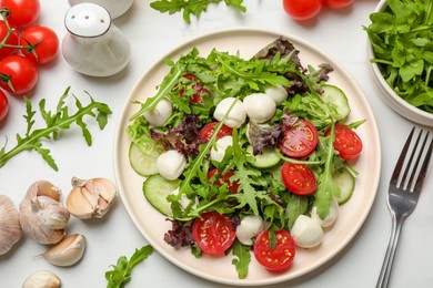 Photo of Tasty salad with arugula, lettuce, mozzarella cheese, vegetables and fork on white table, flat lay