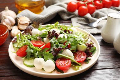 Photo of Tasty salad with arugula, lettuce, mozzarella cheese and vegetables on wooden table, closeup