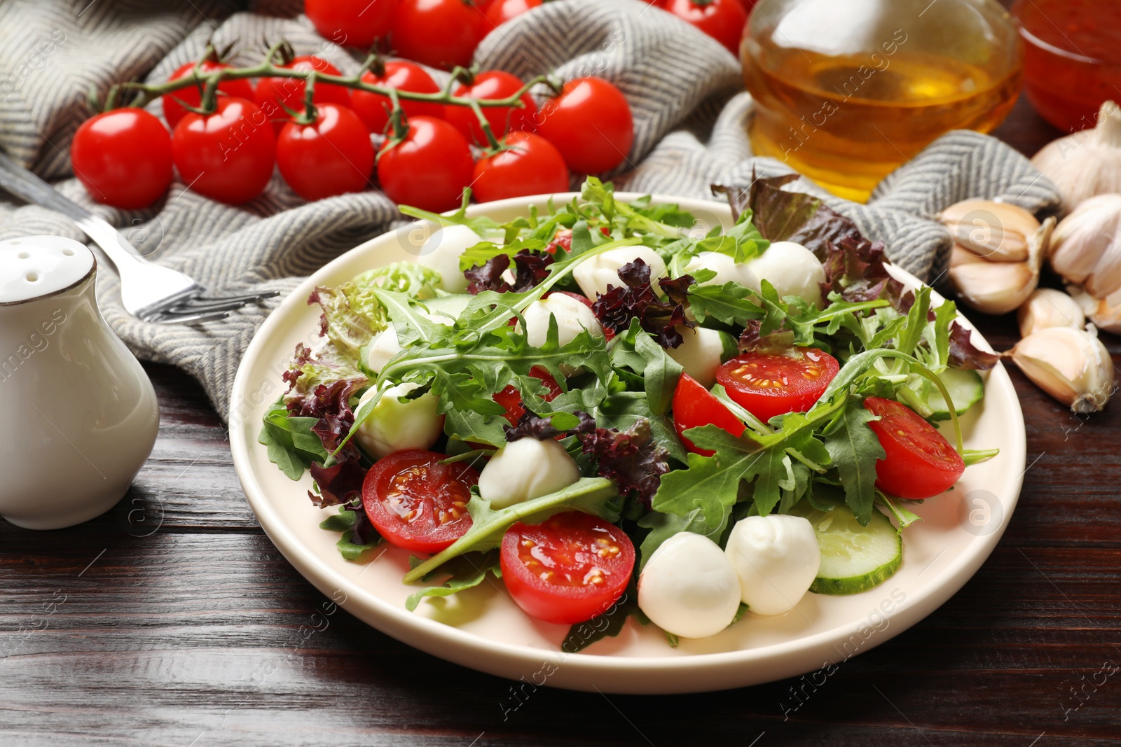 Photo of Tasty salad with arugula, lettuce, mozzarella cheese and vegetables on wooden table, closeup