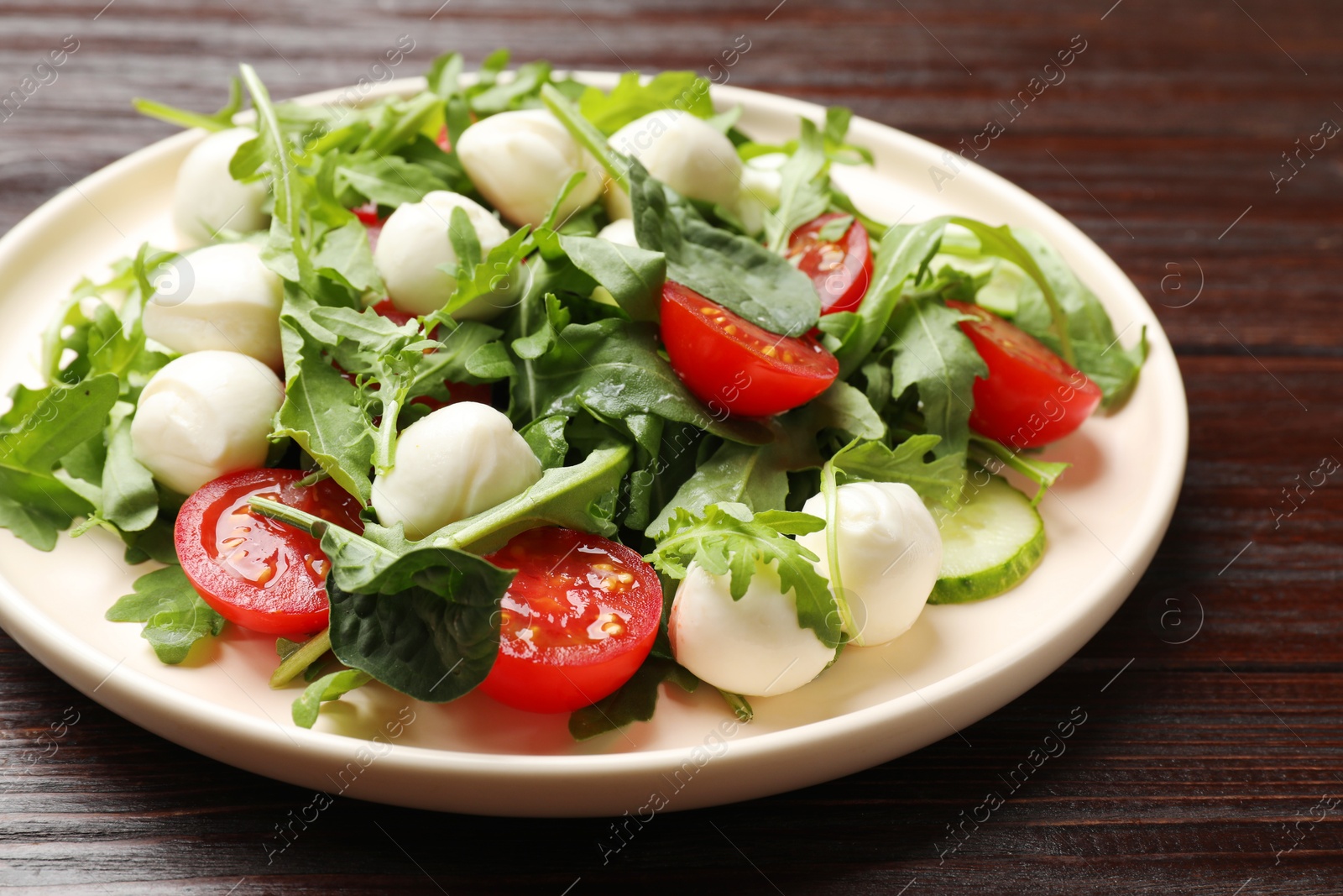 Photo of Tasty salad with arugula, spinach, mozzarella cheese and vegetables on wooden table, closeup