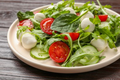 Photo of Tasty salad with arugula, spinach, mozzarella cheese and vegetables on wooden table, closeup