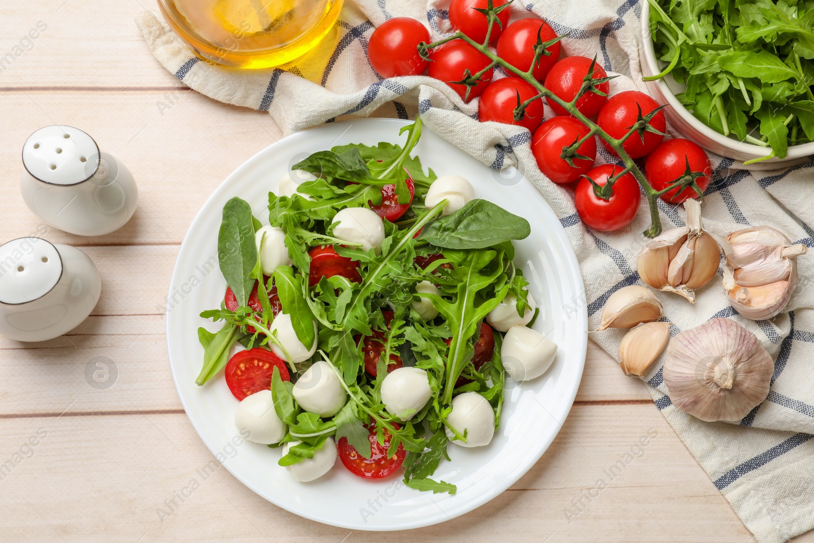 Photo of Tasty salad with arugula, spinach, mozzarella cheese and tomatoes on wooden table, flat lay