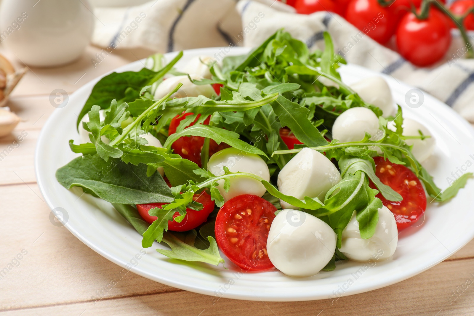 Photo of Tasty salad with arugula, spinach, mozzarella cheese and tomatoes on wooden table, closeup