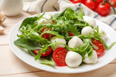 Photo of Tasty salad with arugula, spinach, mozzarella cheese and tomatoes on wooden table, closeup